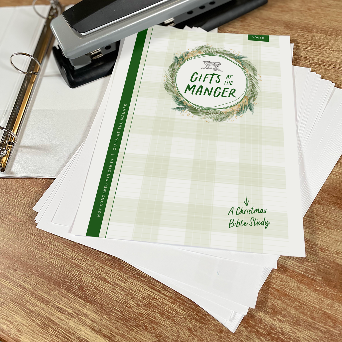 Stack of &#39;Gifts in the Manger&#39; booklets on a wooden surface with stationery items.