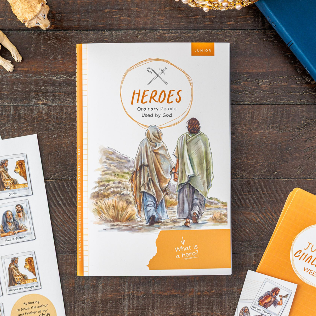 Book titled 'HEROES: Ordinary People Used by God' on a wooden surface with other related materials.